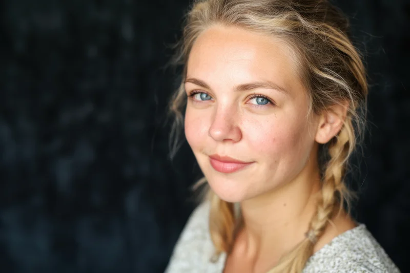 Young woman with blue eyes and blonde hair in a braid smiling softly in a studio portrait