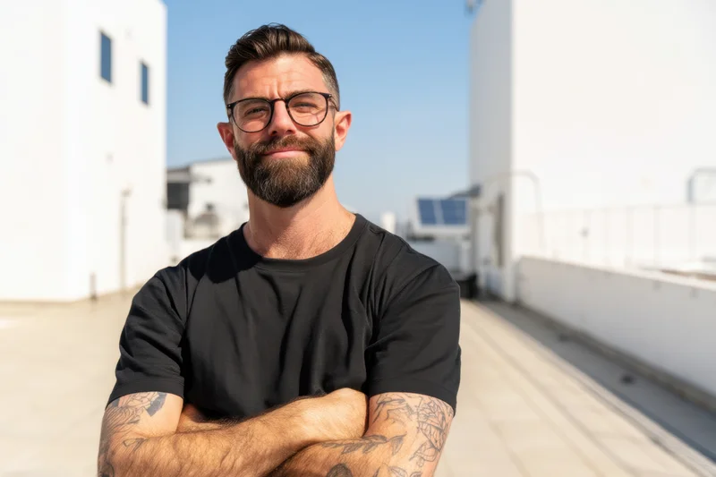 Confident man with beard and glasses standing on rooftop with arms crossed