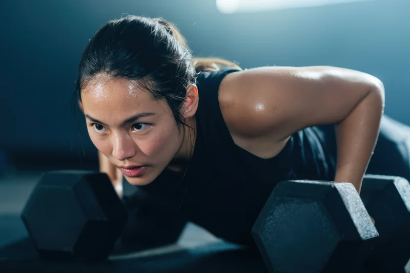 Woman performing push-up with dumbbells in gym