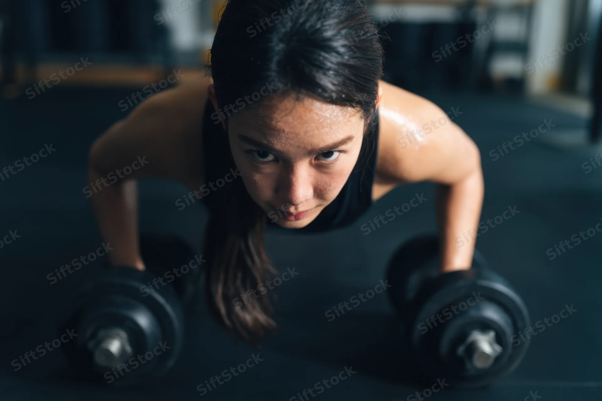 Woman doing push-up with dumbbells in gym