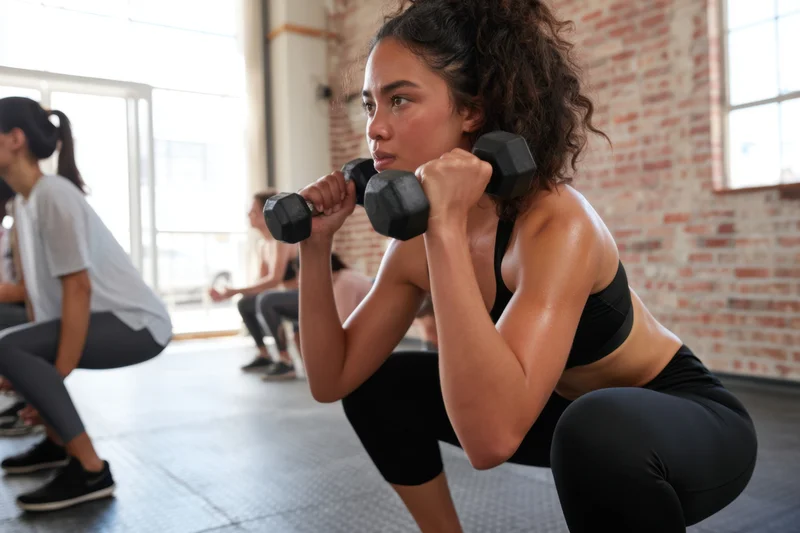 Woman squatting with dumbbells in a gym class