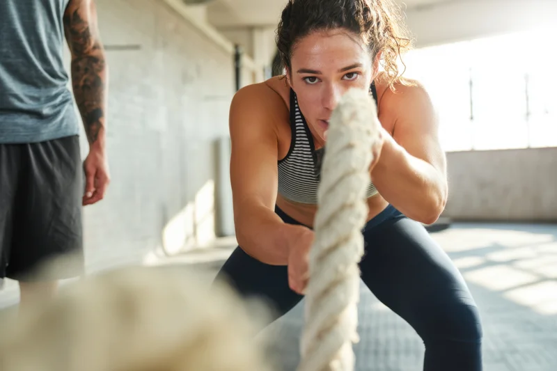 Woman pulling thick rope during intense workout in gym