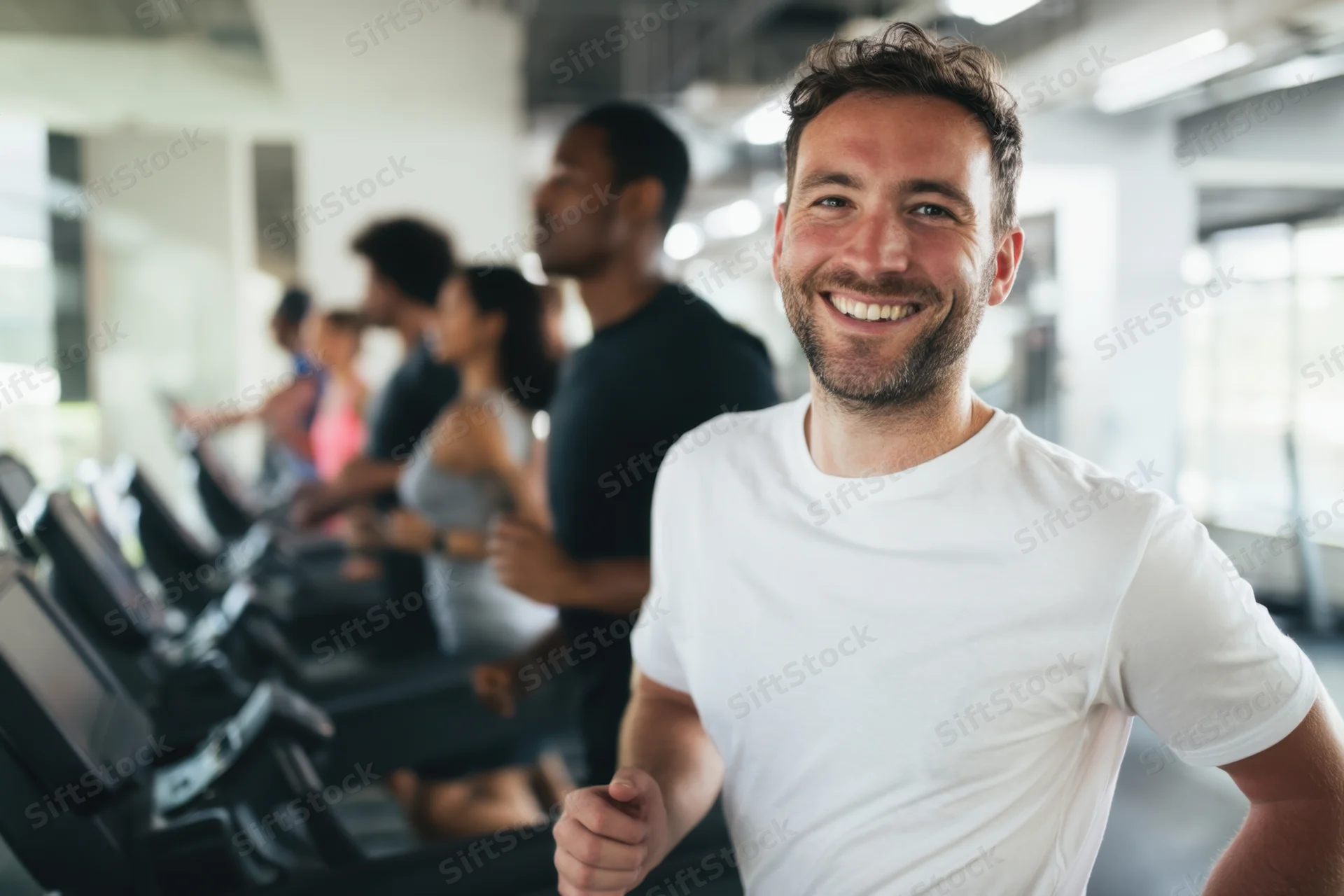 Man smiling while running on treadmill in gym with group behind him