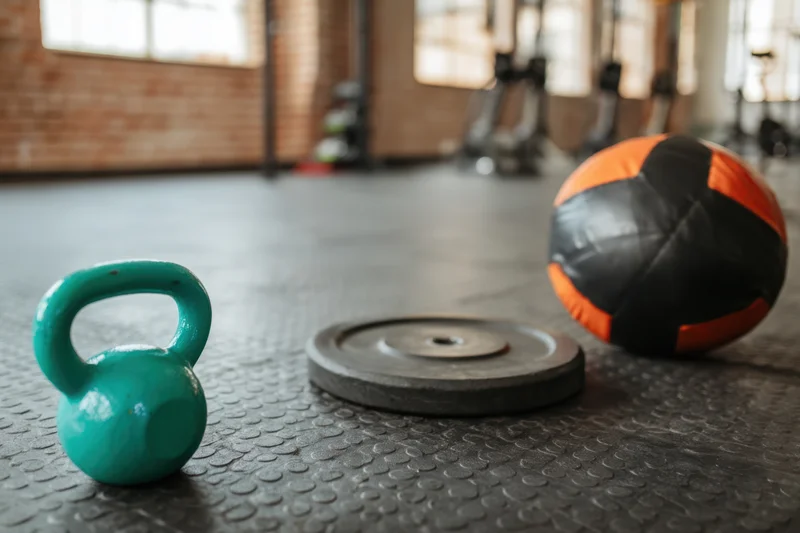Teal kettlebell, barbell plate and orange medicine ball on textured gym floor