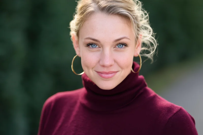 Woman with blonde hair in a maroon turtleneck smiling at camera outdoors