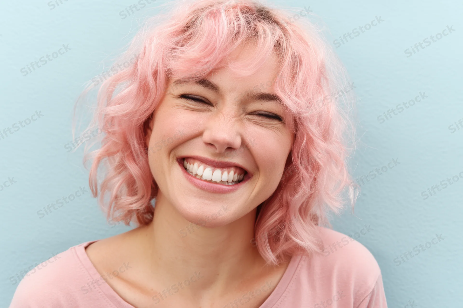 Woman with pastel pink curly hair smiling joyfully in closeup against blue background