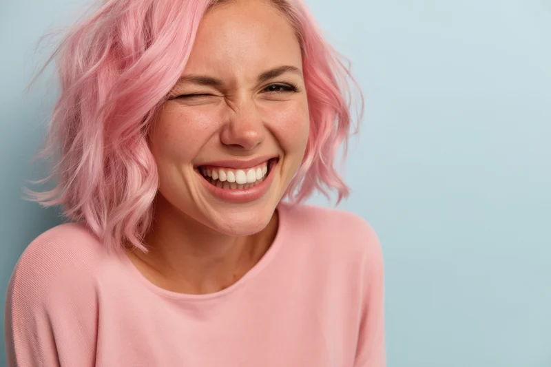 Woman with pastel pink hair smiling joyfully in a studio portrait