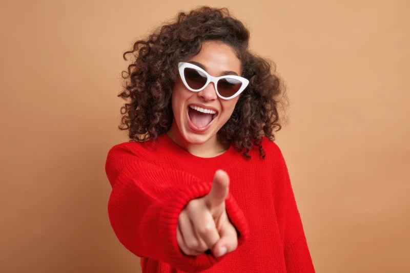Woman in red sweater pointing finger with joyful expression against beige background
