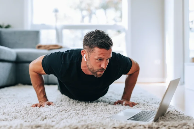 Man doing pushups on carpet in front of laptop in living room