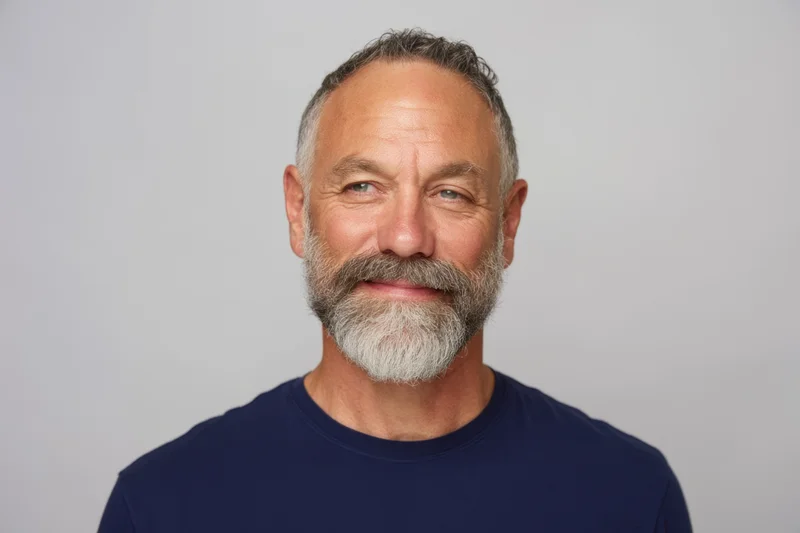 Middle-aged man with salt-and-pepper beard smiling in navy t-shirt against white background