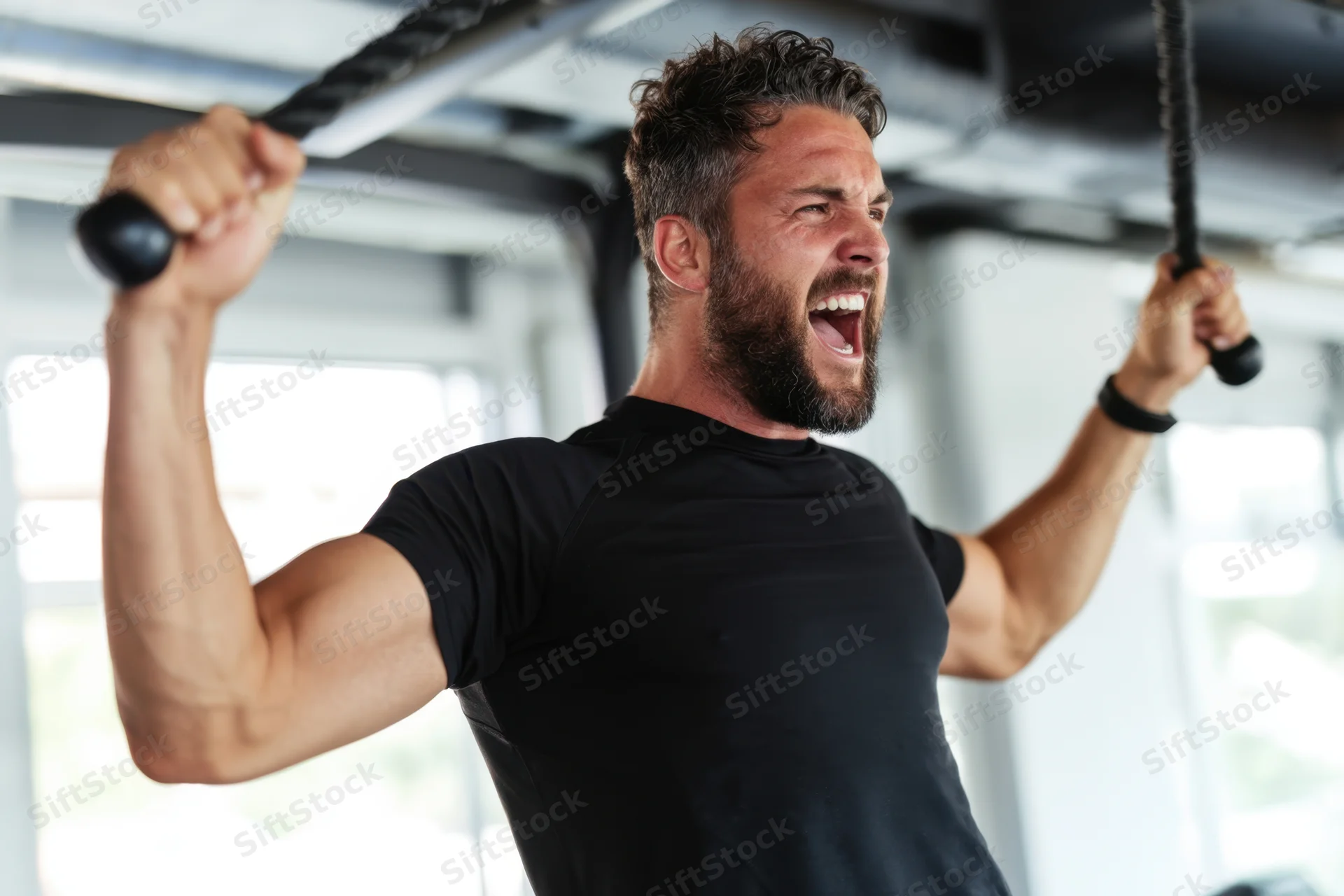 Muscular man pulling cable machine handles in gym with intense expression