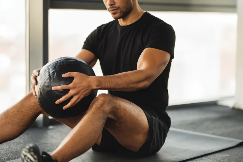 Man sitting on gym mat holding medicine ball during workout