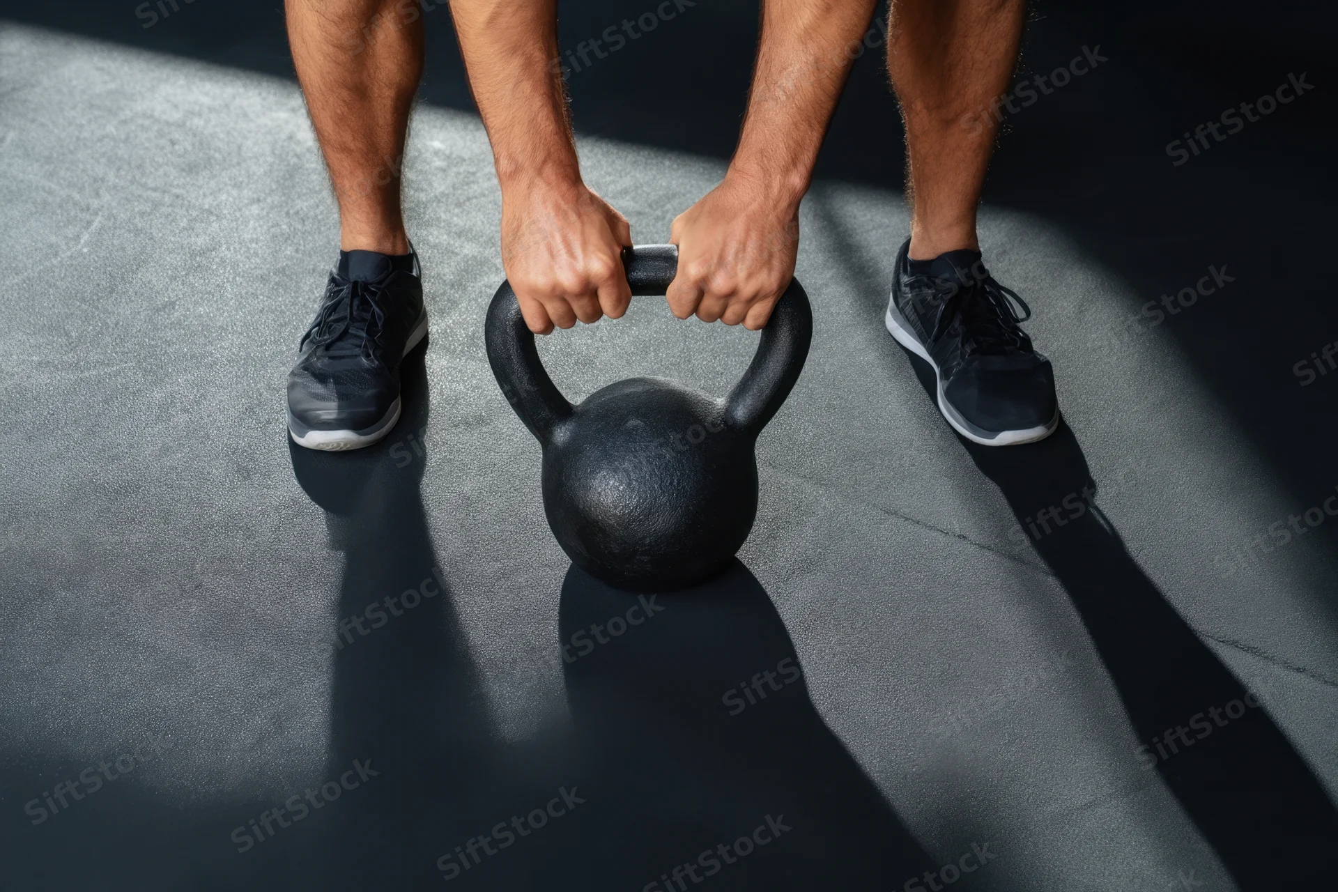 Man gripping kettlebell on gym floor during strength training