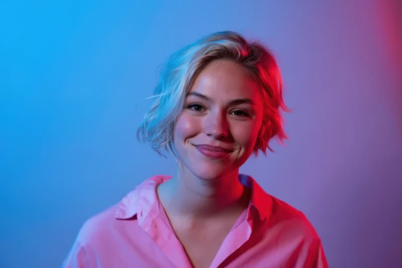 Young woman with short blonde hair smiling in studio under blue and pink neon lighting