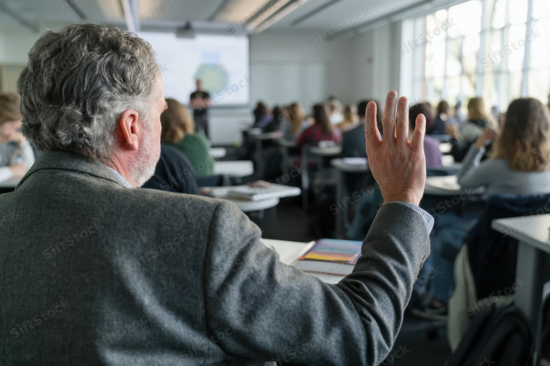 Senior man raising hand in seminar classroom during presentation