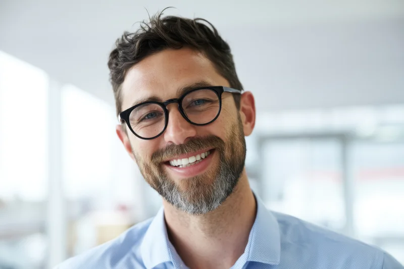 Smiling man with glasses and trimmed beard wearing blue shirt in office setting