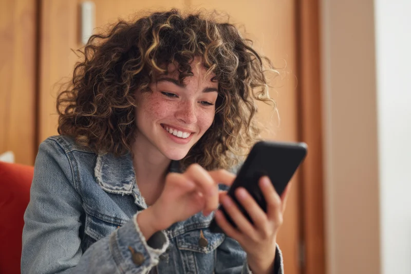 Young woman smiling while using smartphone indoors