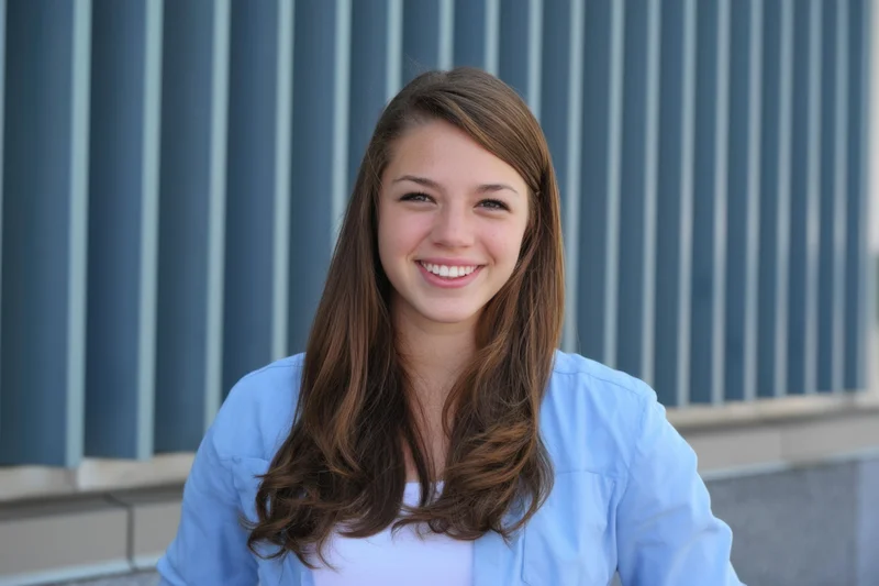 Young woman smiling at camera in front of blue striped building facade
