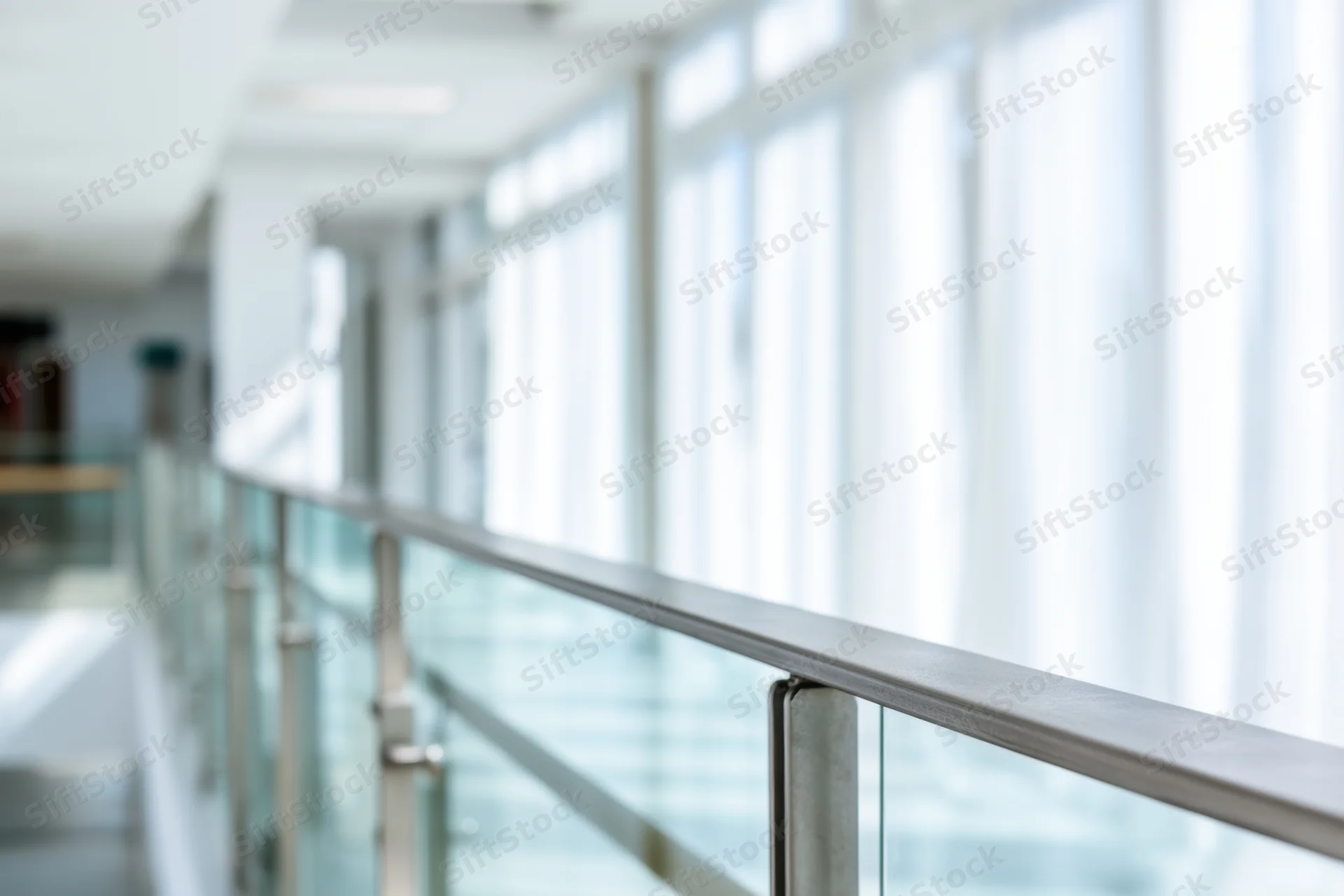 Glass railing along a bright modern office hallway with soft focus background