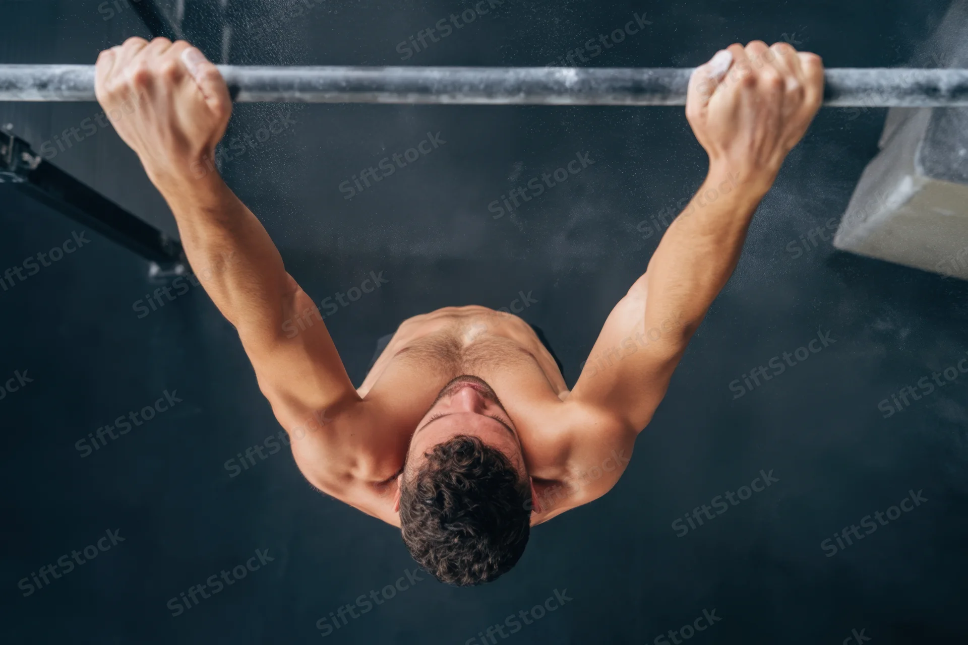 Shirtless man performing pullup on horizontal bar in gym