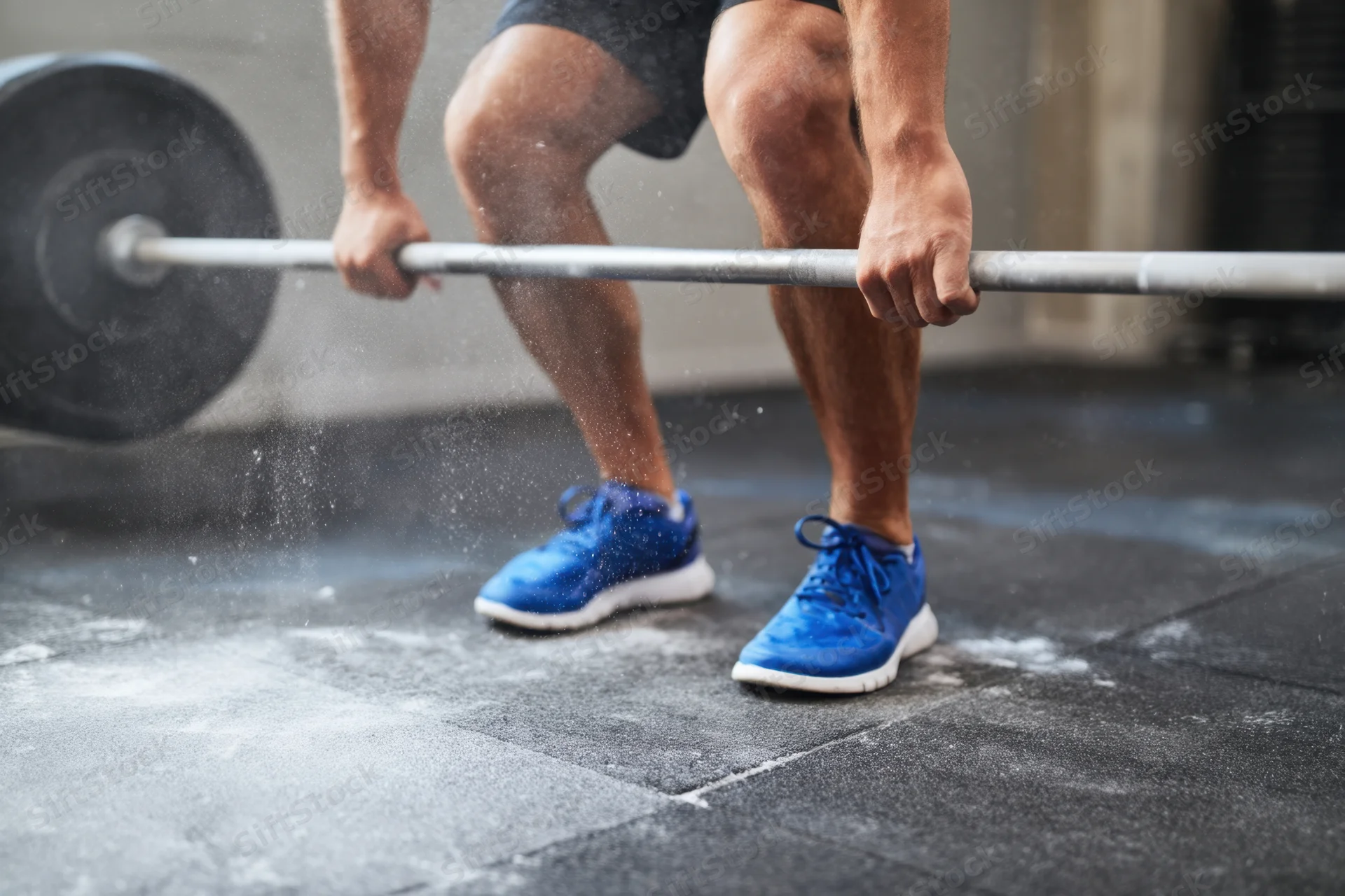 Weightlifter crouching to lift barbell on gritty gym floor
