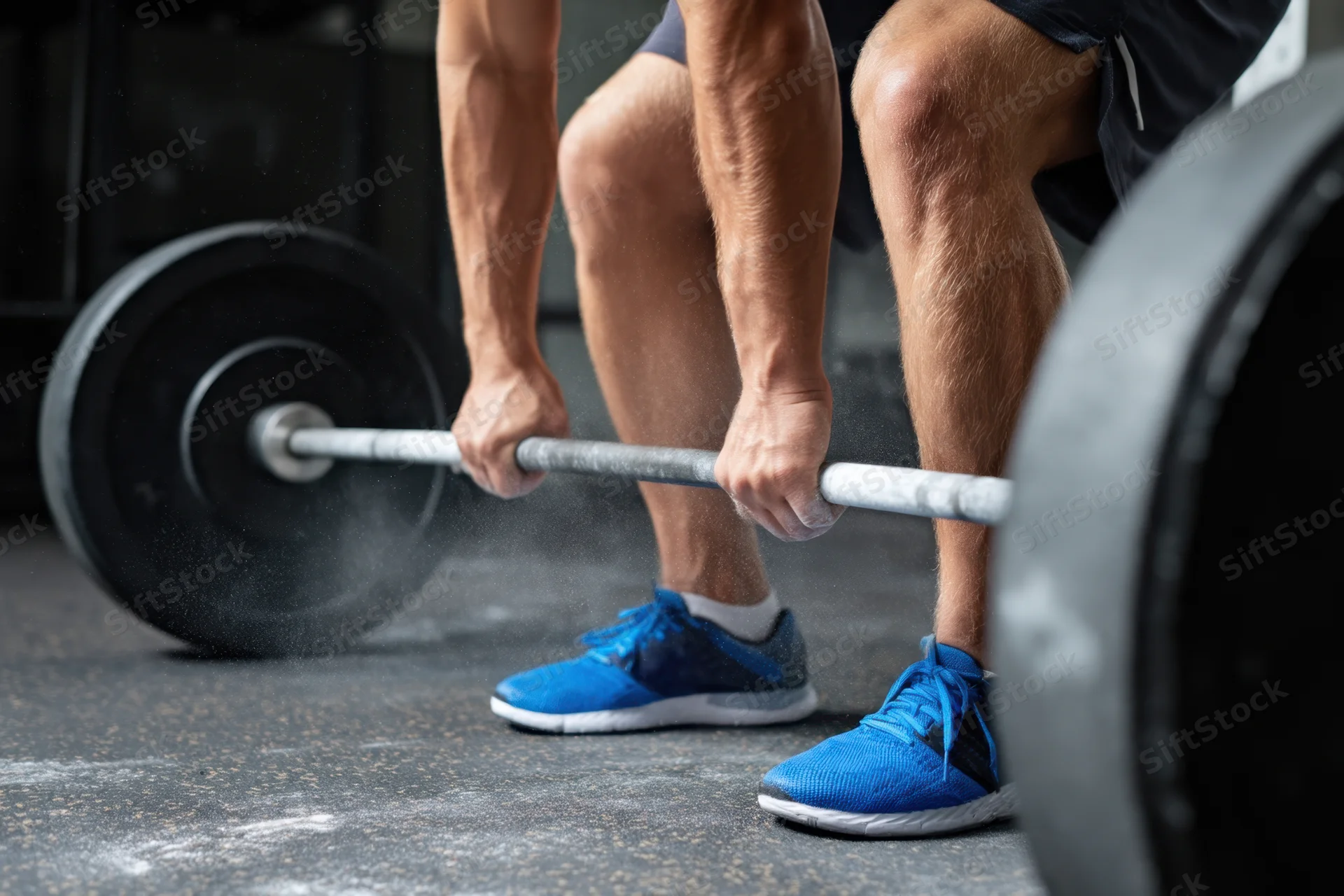 Weightlifter crouching to lift barbell on gritty gym floor