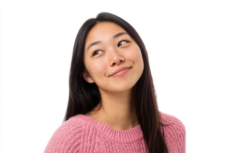 Young asian woman smiling thoughtfully in pink knit sweater against white background