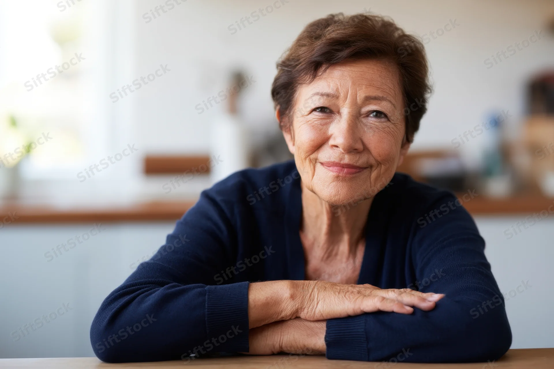 Senior woman smiling with arms crossed at kitchen table