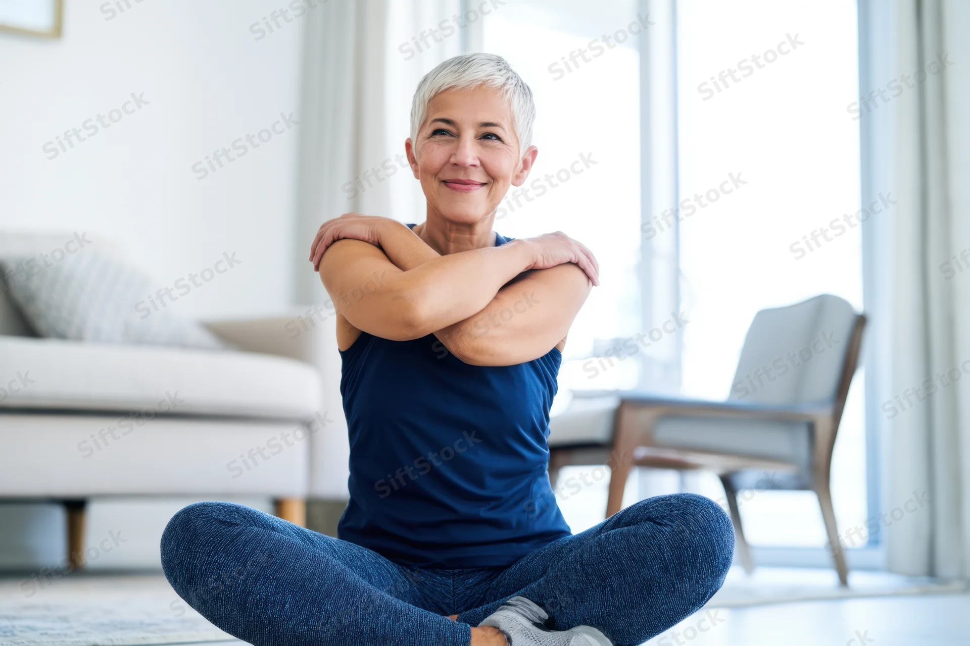 Senior woman stretching in cross-legged position on floor in living room