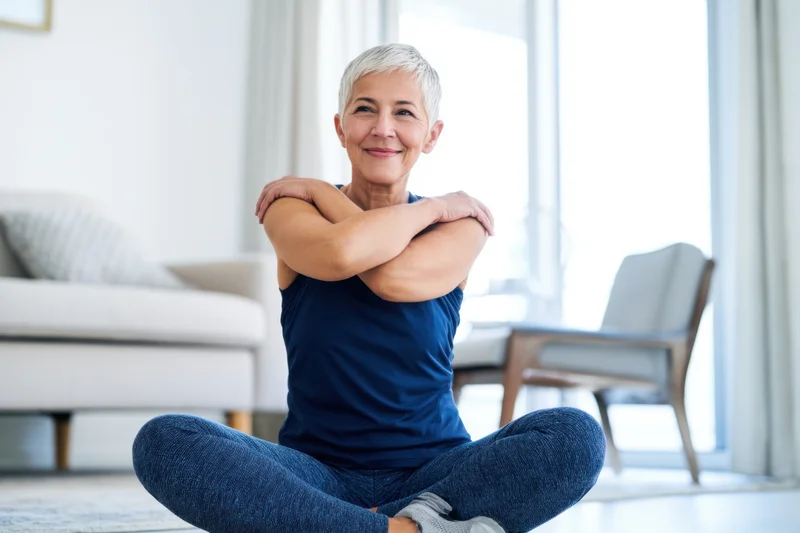 Senior woman stretching in cross-legged position on floor in living room