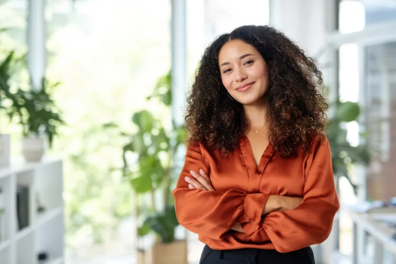 Confident woman with arms crossed smiling in modern office interior