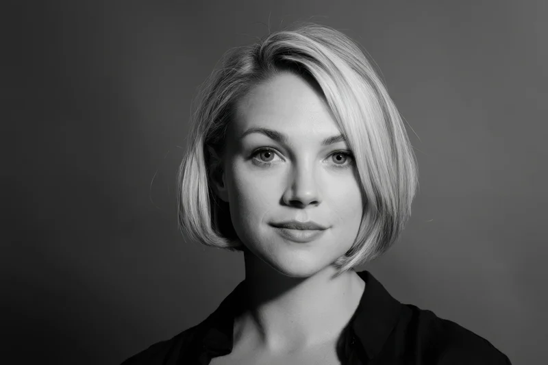 Woman with short blonde bob in black shirt posing for studio portrait with neutral expression