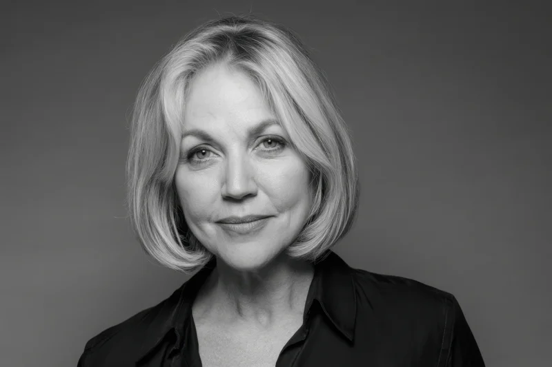 Woman with short blonde hair smiling in a black collared shirt against a neutral gray background