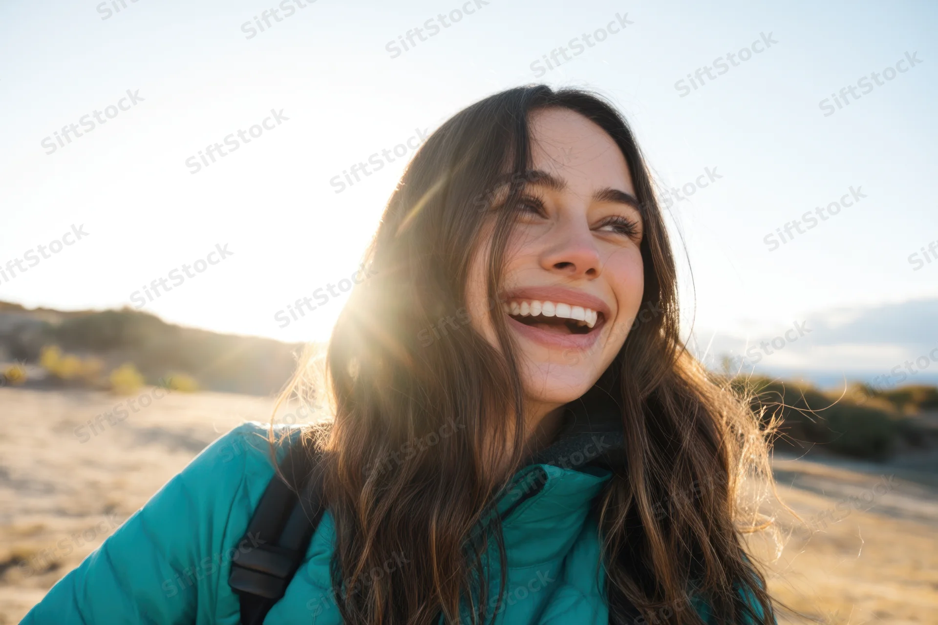Woman smiling outdoors in teal jacket with sun flare and warm light