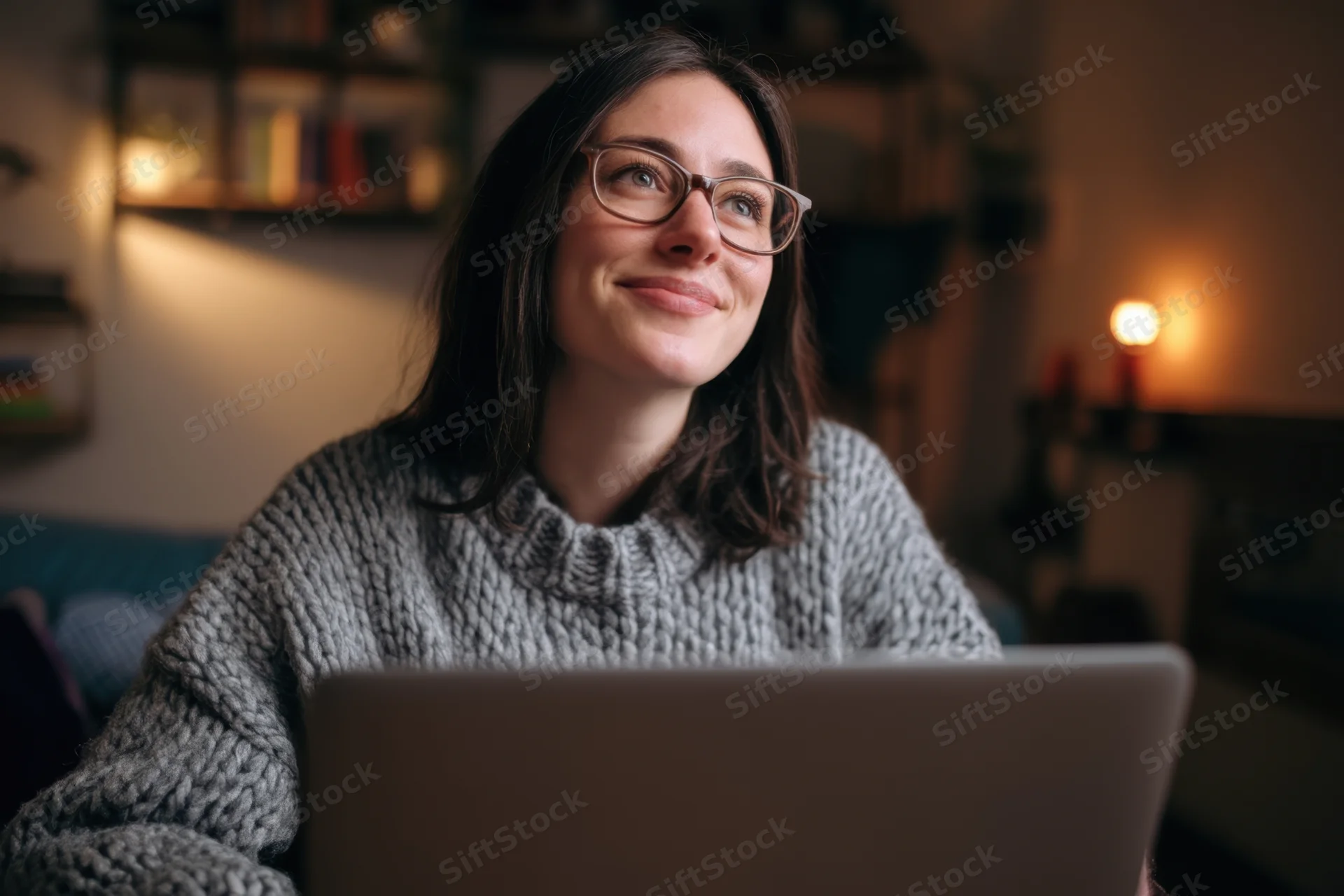 Woman smiling while using laptop at home in cozy evening setting