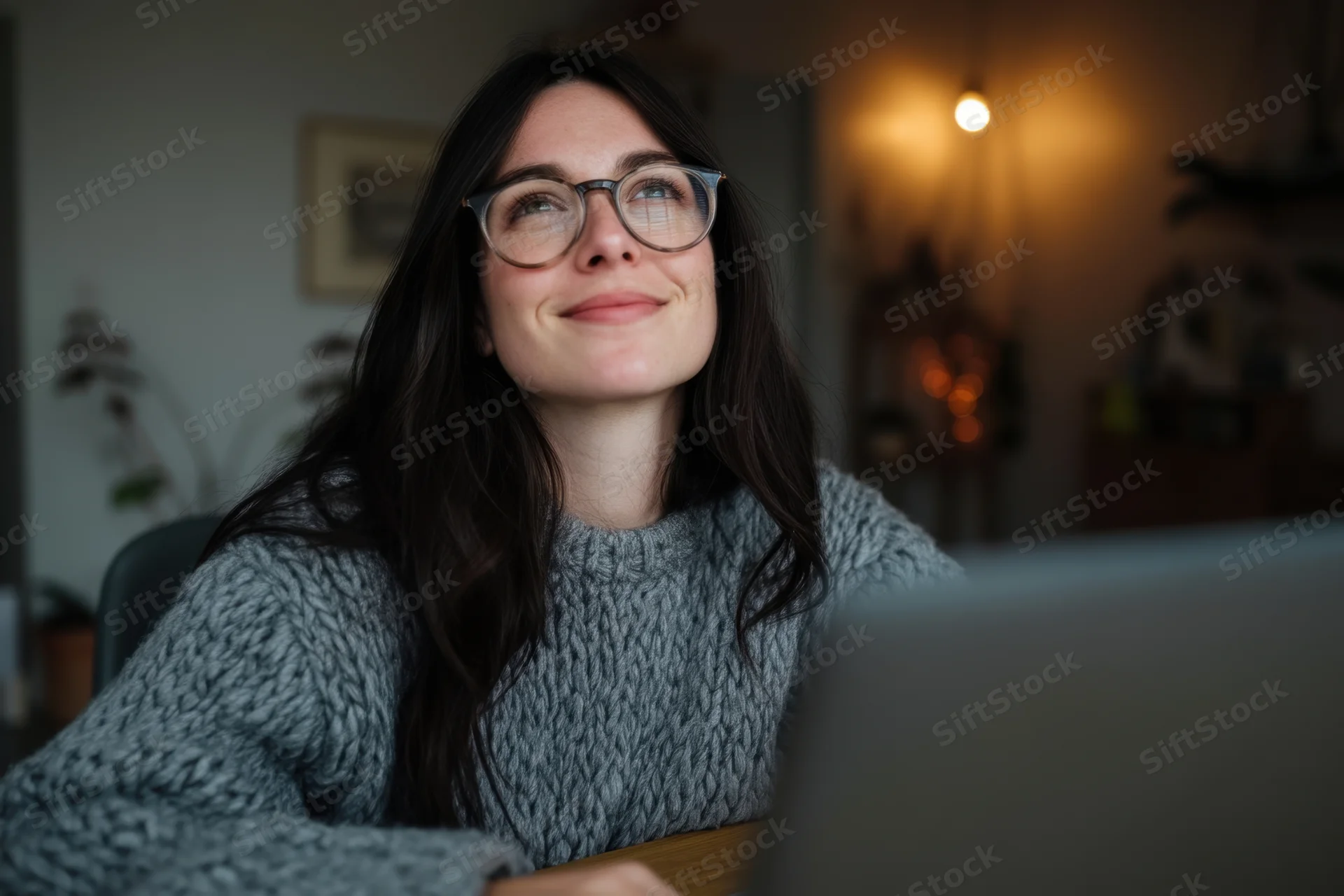 Woman smiling while working on laptop at home desk in evening light