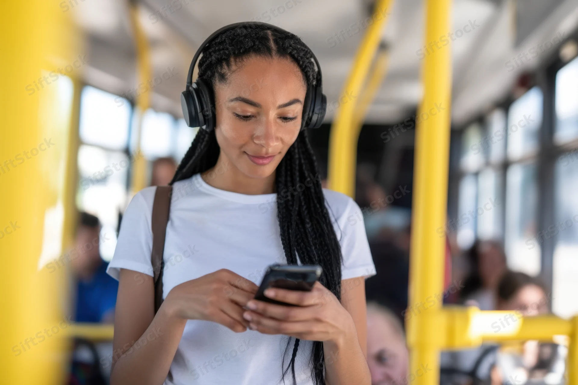 Young woman with braids wearing headphones and using smartphone on a bus
