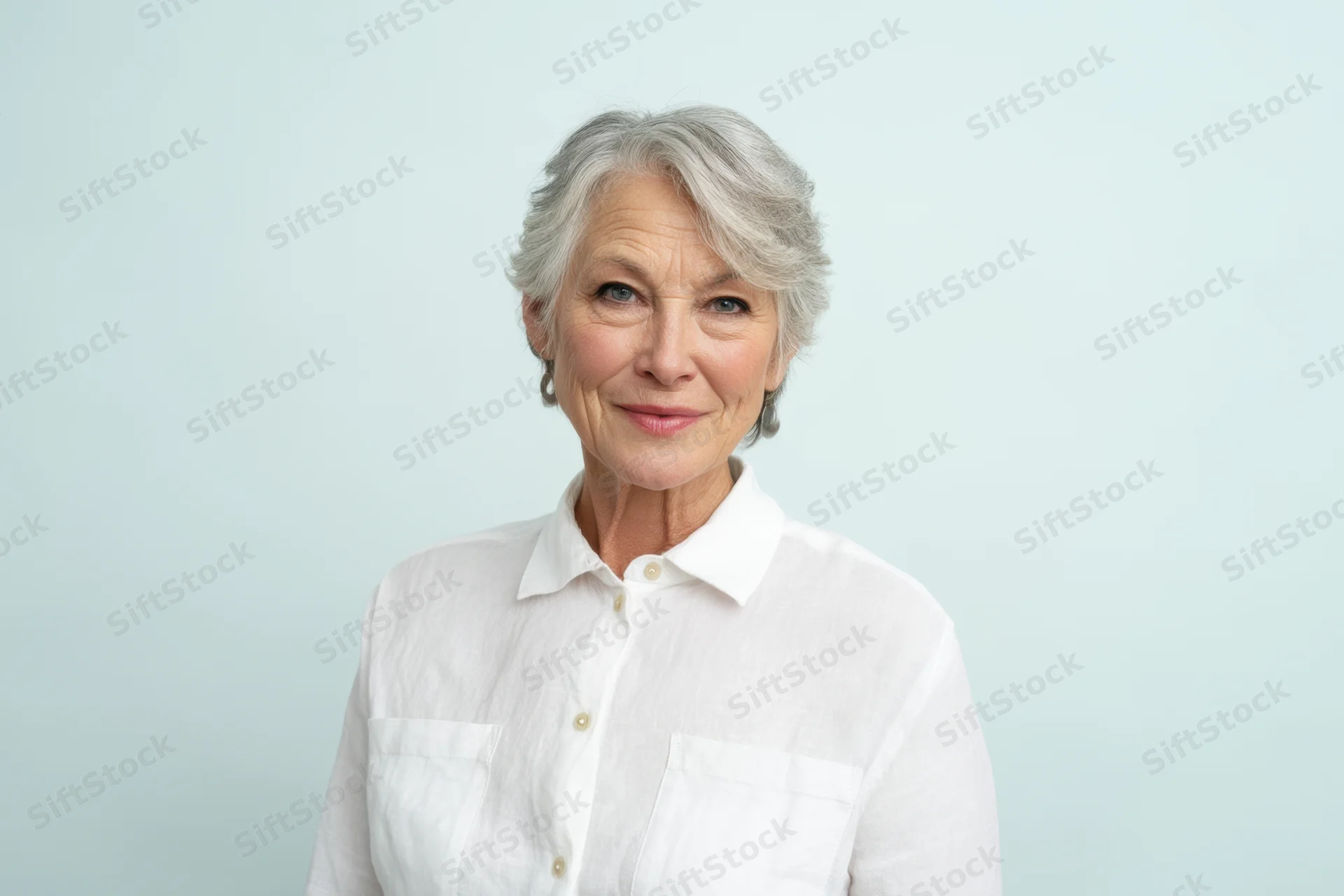 Senior woman in white collared shirt smiling at camera against light blue background