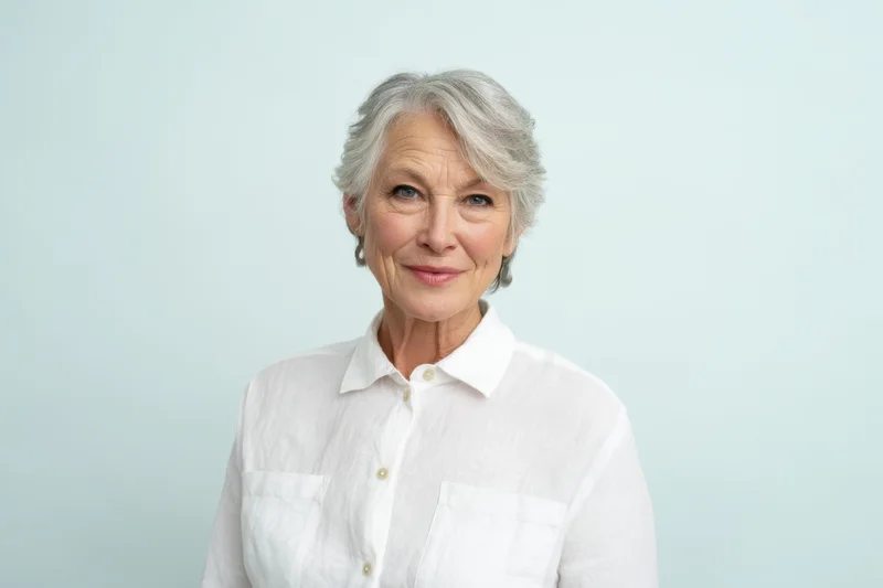 Senior woman in white collared shirt smiling at camera against light blue background