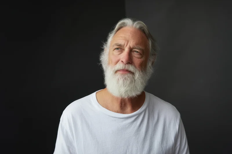 Senior man with full white beard and silver hair wearing white tshirt in studio portrait