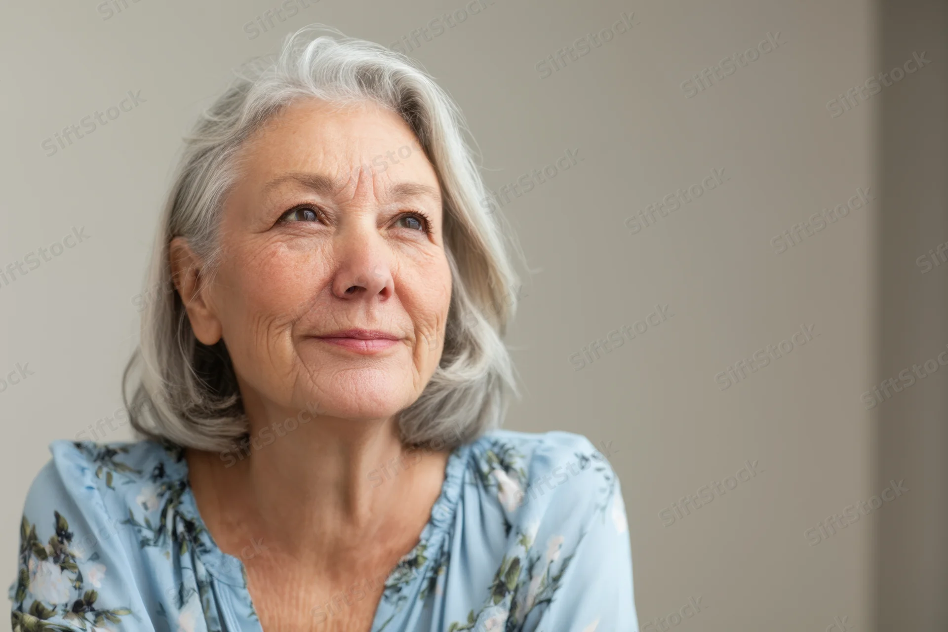 Senior woman with shoulder-length gray hair smiling gently while looking upward in a studio portrait