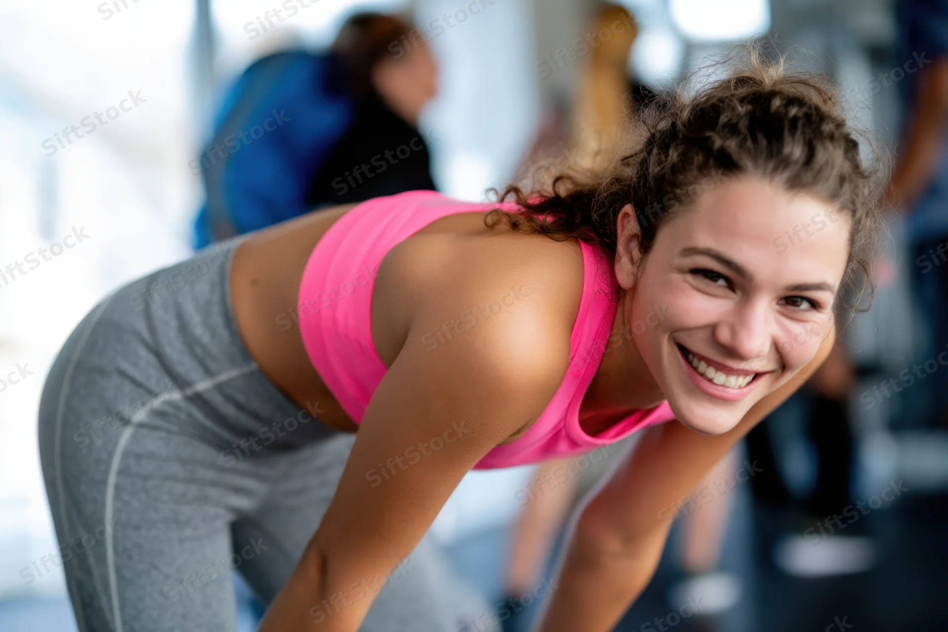 Fit woman smiling with hands on knees after workout in gym