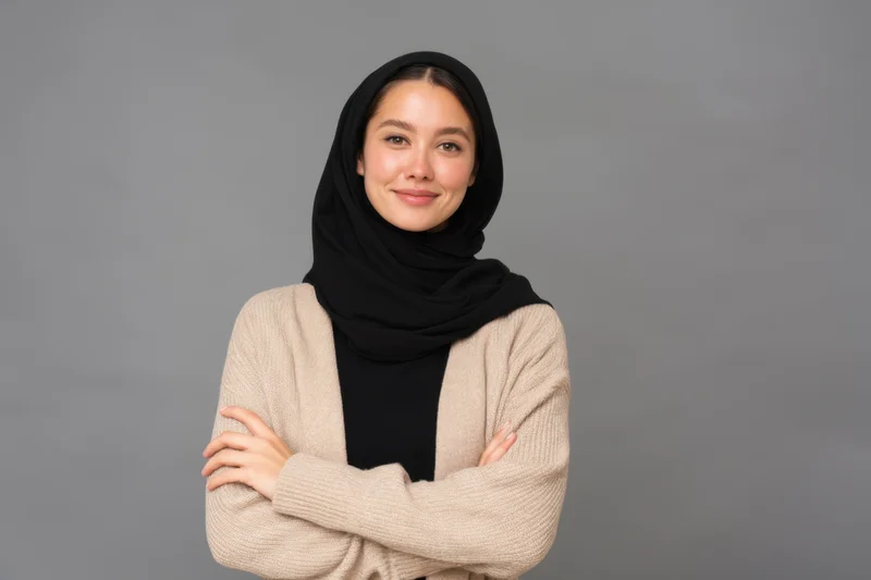 Woman wearing black hijab and beige cardigan with arms crossed in studio portrait