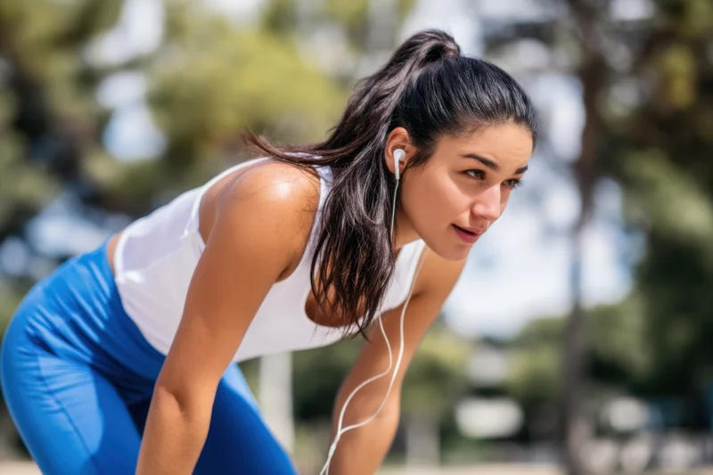 Woman bending forward after exercise in a park wearing earphones and athletic clothing