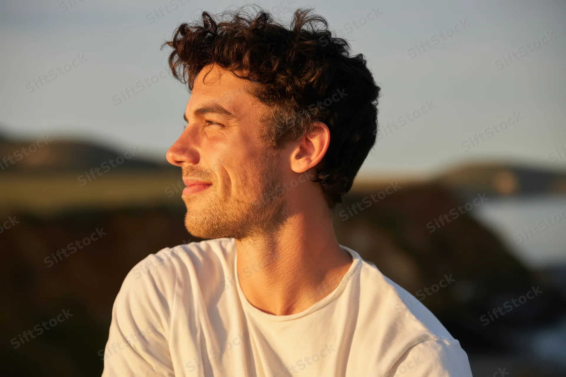 Young man smiling in profile outdoors at sunset near the coast
