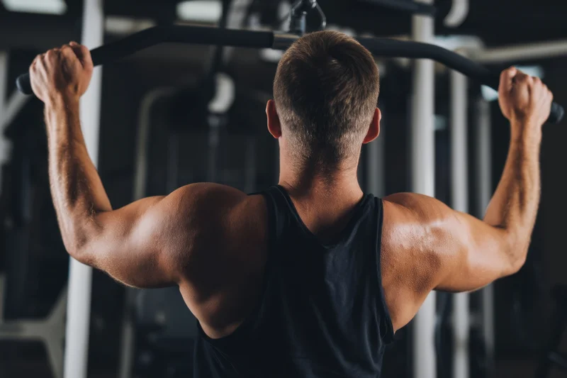 Muscular man pulling cable in gym from behind
