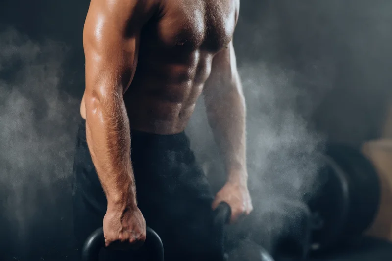 Muscular man gripping kettlebells in a smoky gym