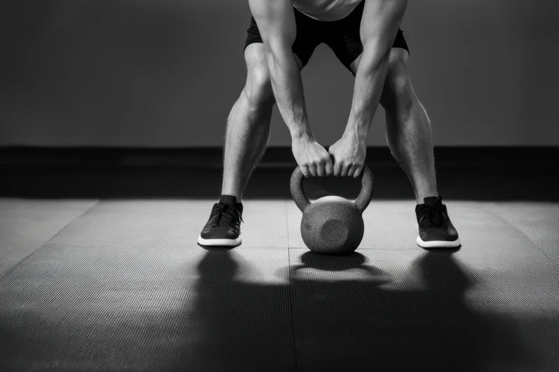 Man gripping kettlebell in low squat position on gym floor