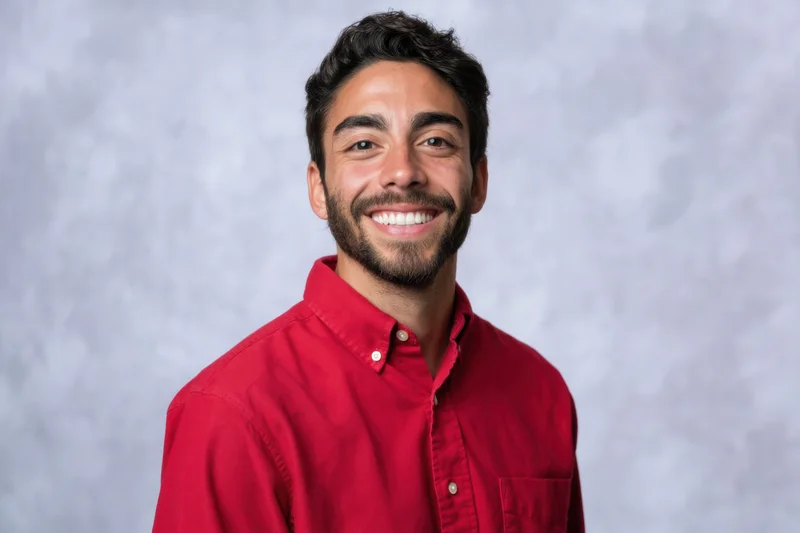Young man smiling in a red button-down shirt against a gray studio backdrop