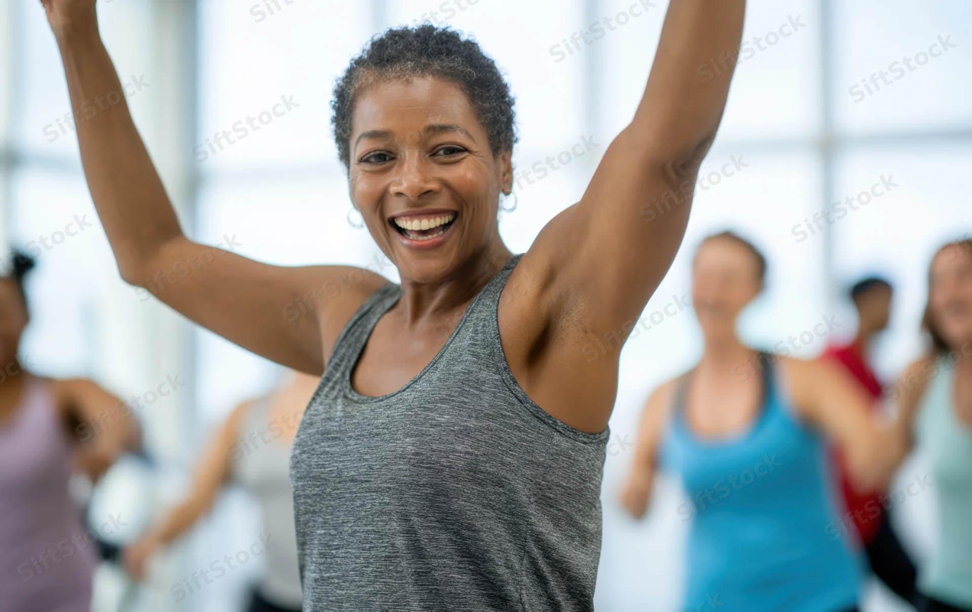 Smiling middle-aged african american woman leading a group fitness class with arms raised in a bright gym